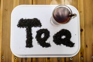 Cup of hot tea on a tray with tea leaves that spell out tea for an ingredient article about Earl Grey tea