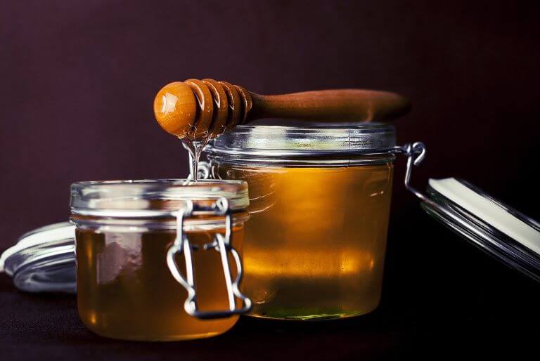Two glass mason jars of honey with honey dipper on top for an ingredient article about new fragrance and flavor products