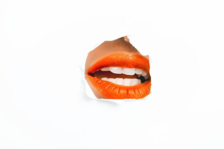 White background with ripped cut out of an opened mouth with bright orange lipstick for an ingredient article about Mastiha, Shiso and Kimchi