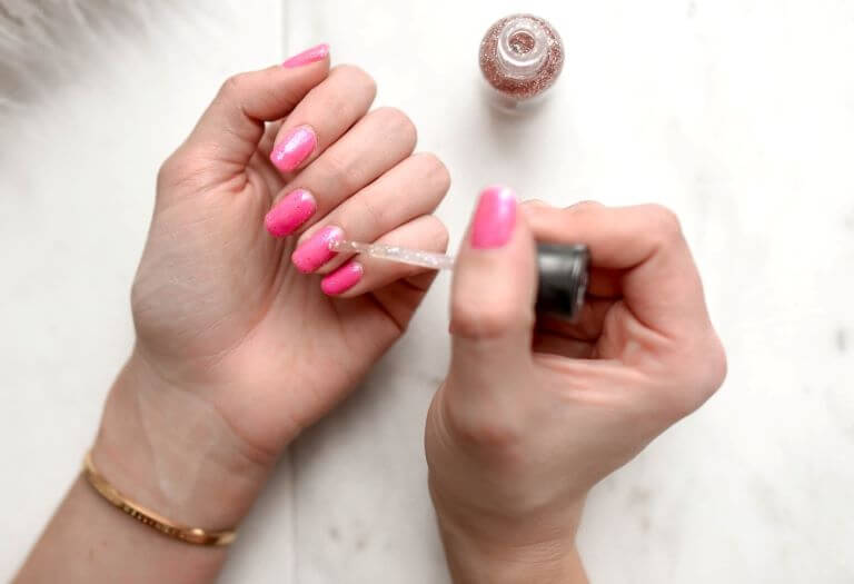 A woman giving herself a manicure with pink glittery nail polish for an article about natural and nontoxic nail polish