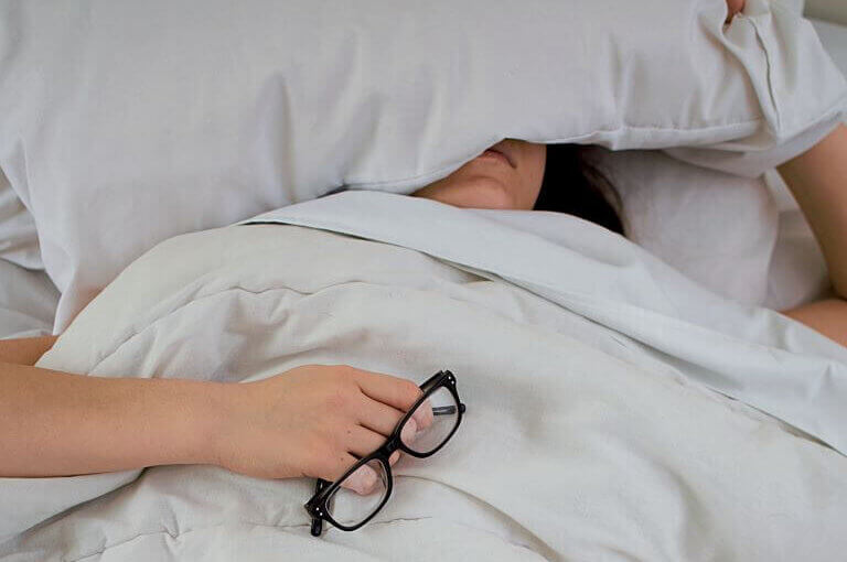 Woman sleeping with pillow on her head and glasses in her hand for trend article on sleep products and relaxing functional food and beverages
