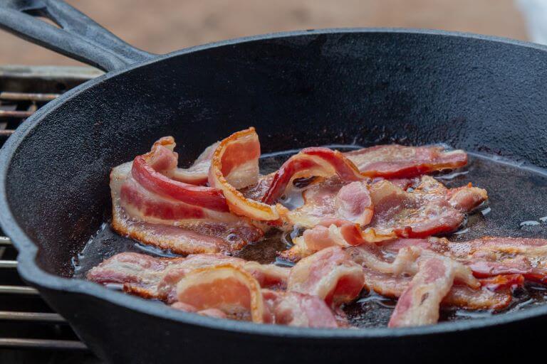 Bacon sizzling in black cast iron pan fro trend article about real and alt bacon