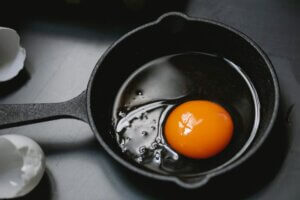 Black iron pan with cracked egg and egg shell next to it for article about plant-based egg alternatives