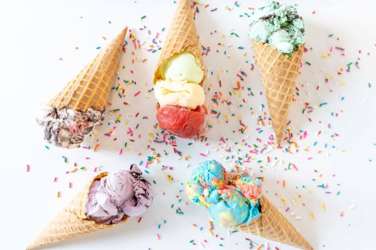 Five colorful ice cream cones with different flavors and sprinkles for a trend article about summer ice cream launches