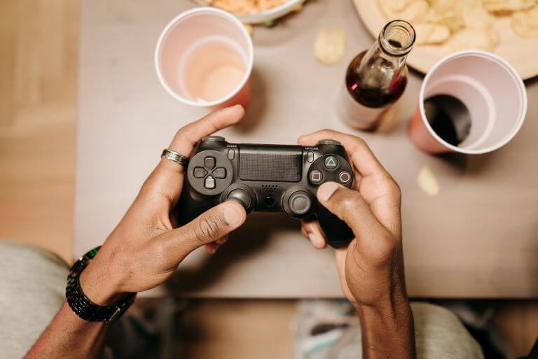 Close up Playstation controller in African American male's had with chips and drink for trend article about gamers as a target audience