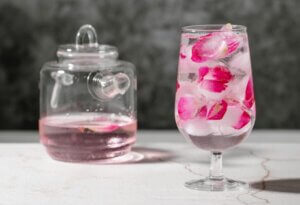 glass teapot with pink beverage and glass with pink floral ice cubes for a trend article about collagen-infused beauty beverages