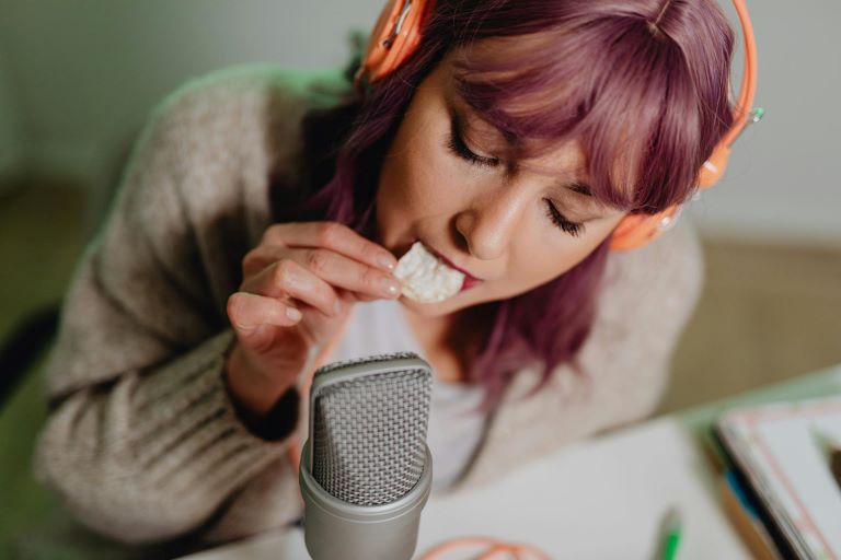 Woman with orange headphones eating a cracker into a microphone for a trend article about sound and texture influencing food and beverage